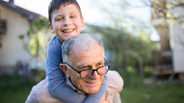 Ein Kind spielt mit seinem Großvater im Garten. Beide lachen und sind glücklich.